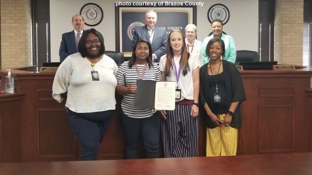 Photo courtesy of Brazos County showing in the front row, employees of the Bryan Adult Protective Services office and in the rear row, members of the Brazos County commissioners court.