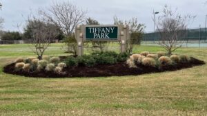 Photo taken March 1, 2024 of the Tiffany Park sign where in the distance behind the sign is a disc golf basket.