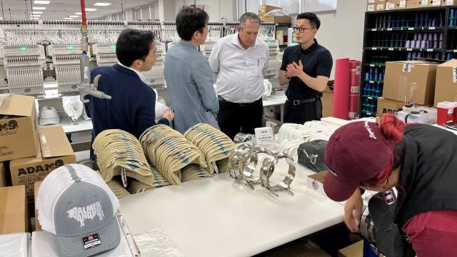 At the far right, Tajima Industries CEO Hidetoshi Kojima visits with C.C. Creations owner Kenny Lawson during a tour of Tajima embroidery machines in operations at the new C.C. Creations Legacy Campus in Bryan TX on June 28, 2024.