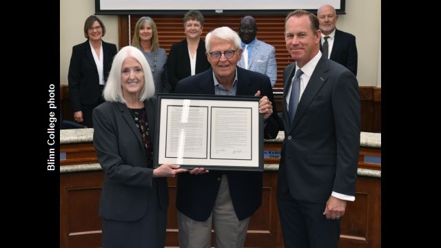 Blinn College photo showing Charles Moser (center) receiving a framed copy of a resolution from (L) chancellor Mary Hensley and (R) trustees chairman Jim Kolkhorst.